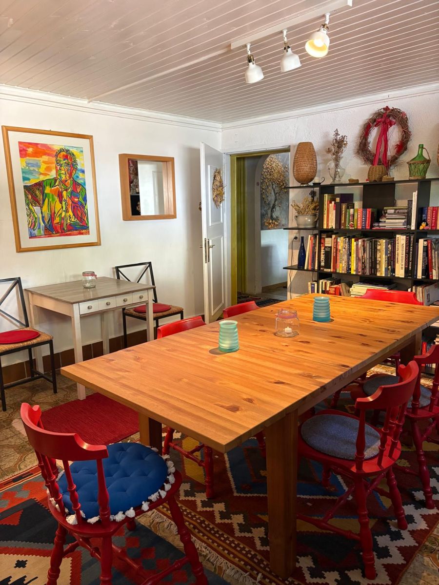 Essraum im Haus Feuchtl mit langem Holztisch und roten Stühlen – ein großes, farbenfrohes Portrait von Franz Feuchtl hängt an der Wand, daneben ein Bücherregal