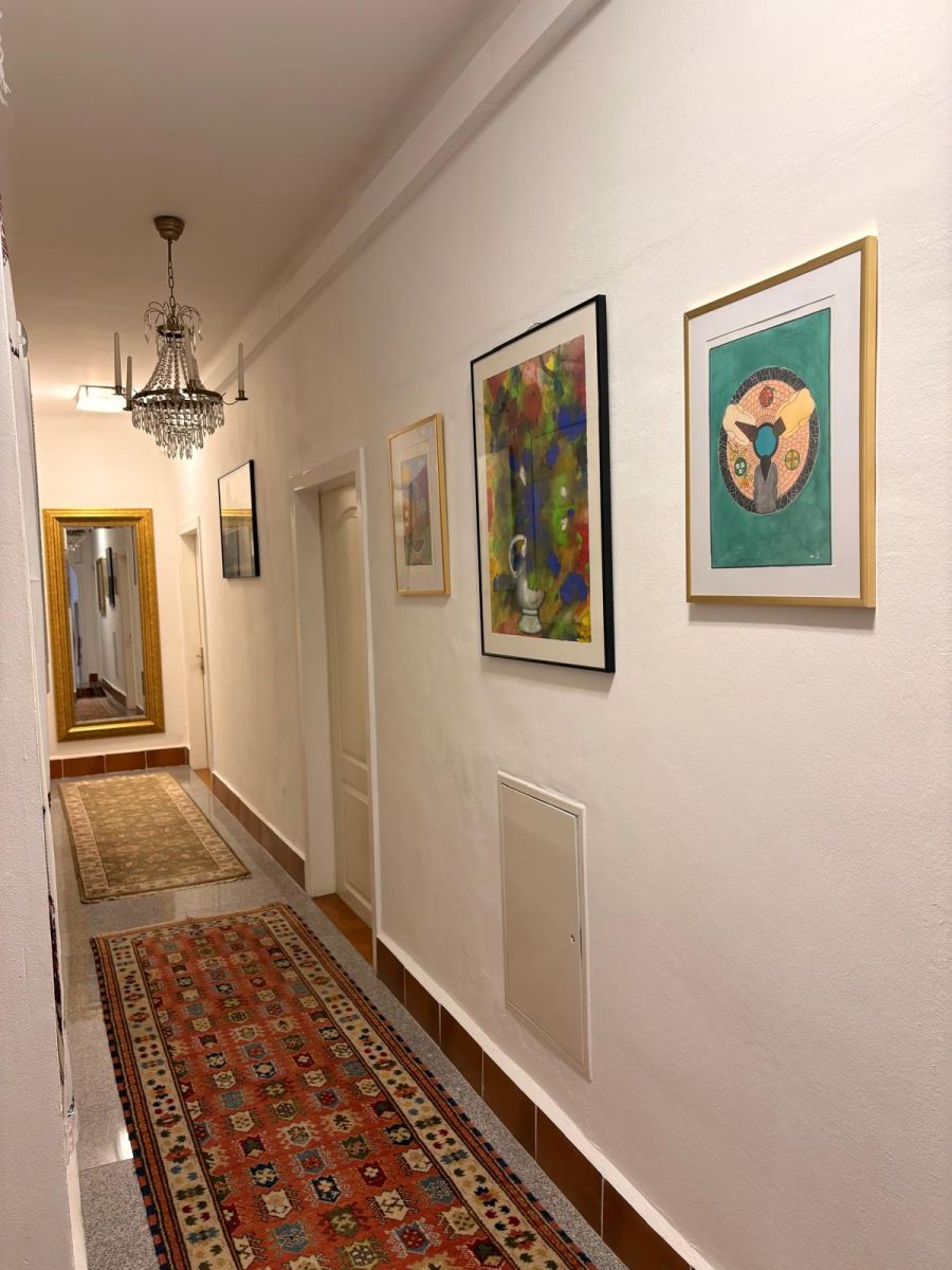 Langer Gang im Haus Feuchtl mit Kronleuchter und orientalischen Teppichen – mehrere gerahmte Werke der Feuchtl Collection hängen an der rechten Wand in Reihe