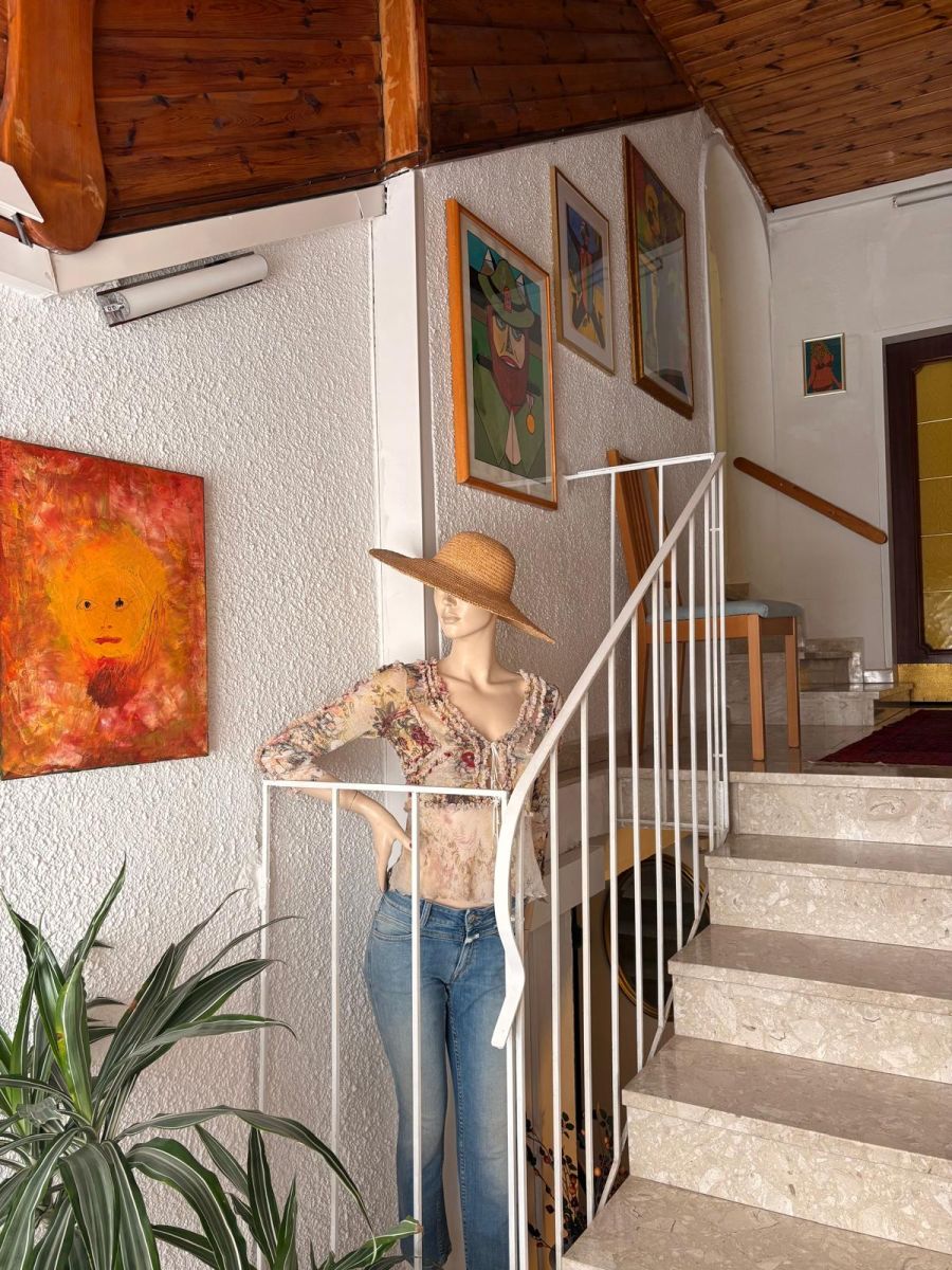 Stiegenaufgang im Haus Feuchtl – mehrere gerahmte Gouachen und ein großes Ölbild von Franz Feuchtl hängen an der Wand neben der Marmorstiege, am Fuß der Treppe eine Schaufensterpuppe